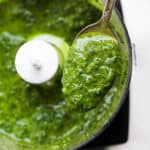 A spoon lifting out some basil vinaigrette out of a small food processor.