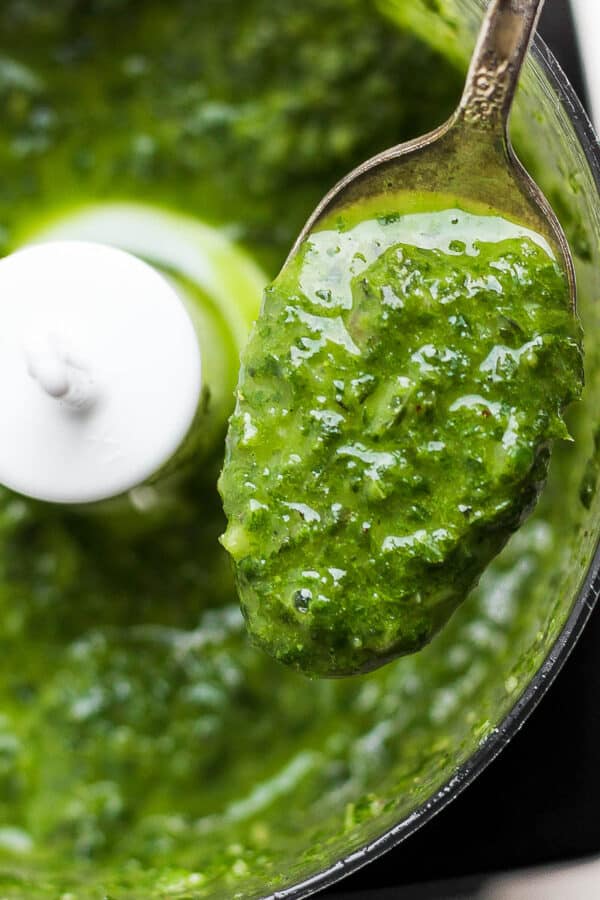 A spoon lifting out some basil vinaigrette out of a small food processor.