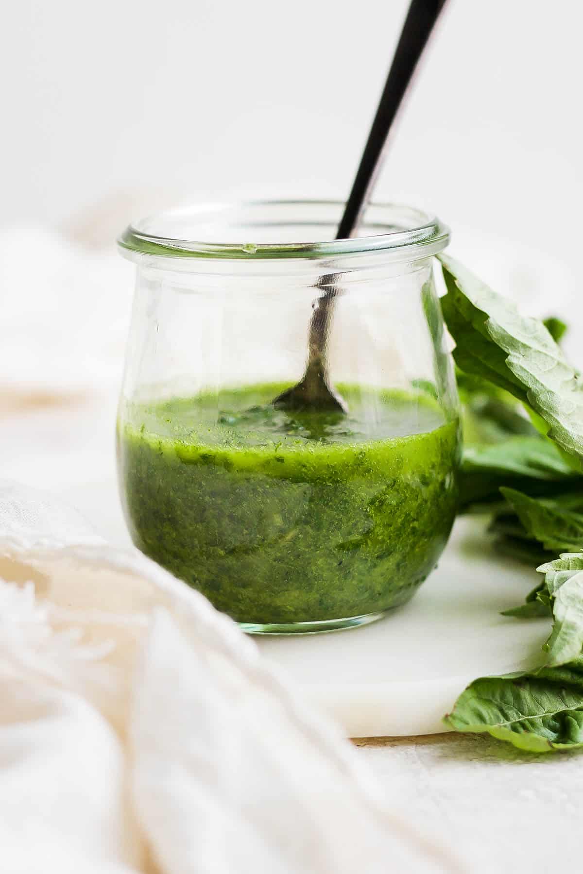 Basil vinaigrette in a small glass jar with a spoon.