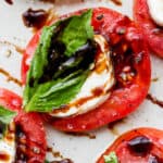 A piece of caprese salad with a fresh tomato slice, slice of fresh mozzarella cheese and fresh basil with balsamic vinegar on top.