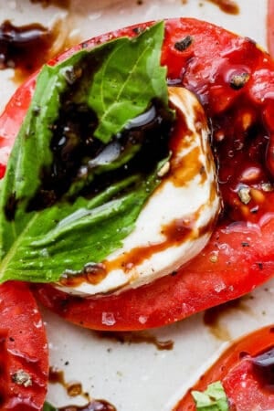 A piece of caprese salad with a fresh tomato slice, slice of fresh mozzarella cheese and fresh basil with balsamic vinegar on top.