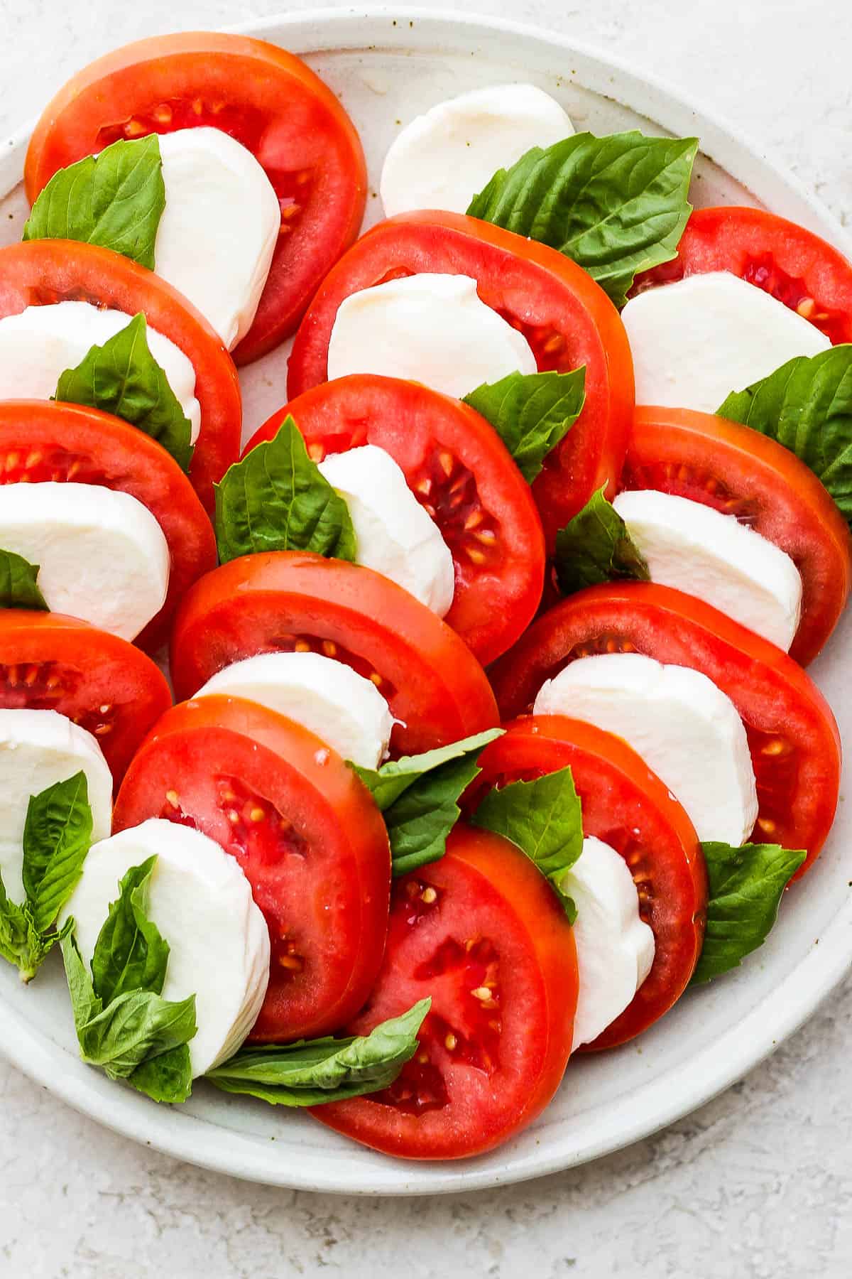 Thick slices of tomato and mozzarella cheese layered with basil leaves on a plate.