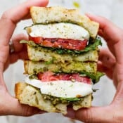 Two hands holding a caprese sandwich that has been cut in half so you can see the inside,