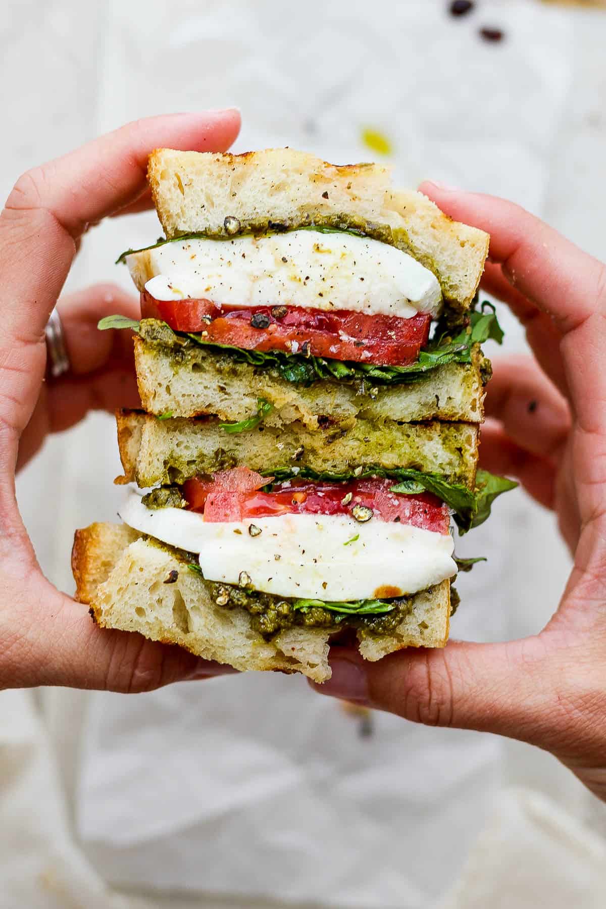 Two hands holding a caprese sandwich that has been cut in half to see the inside.