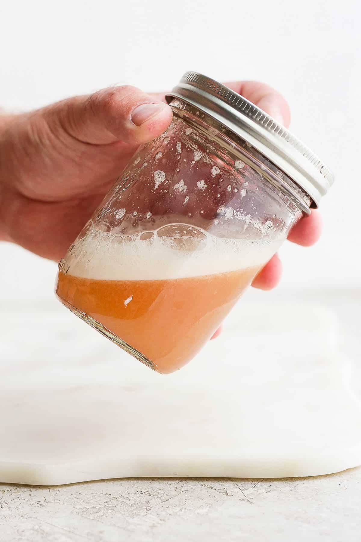 A cranberry orange whiskey sour being shaken in a mason jar.