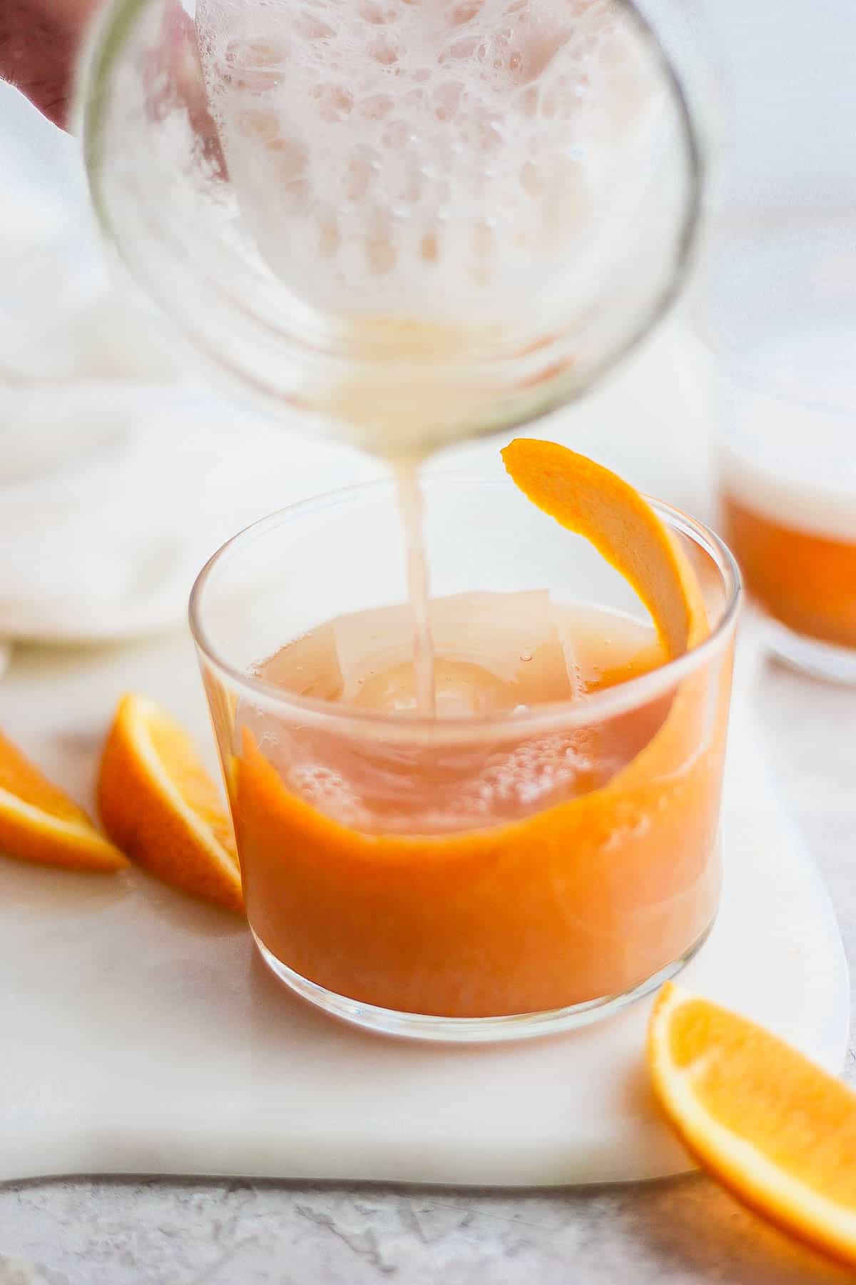 A shaken whiskey sour being poured over ice in a glass.