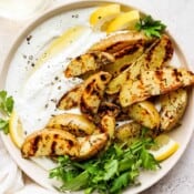 A shallow bowl of whipped feta with garlic potato wedges, lemons and fresh parsley.