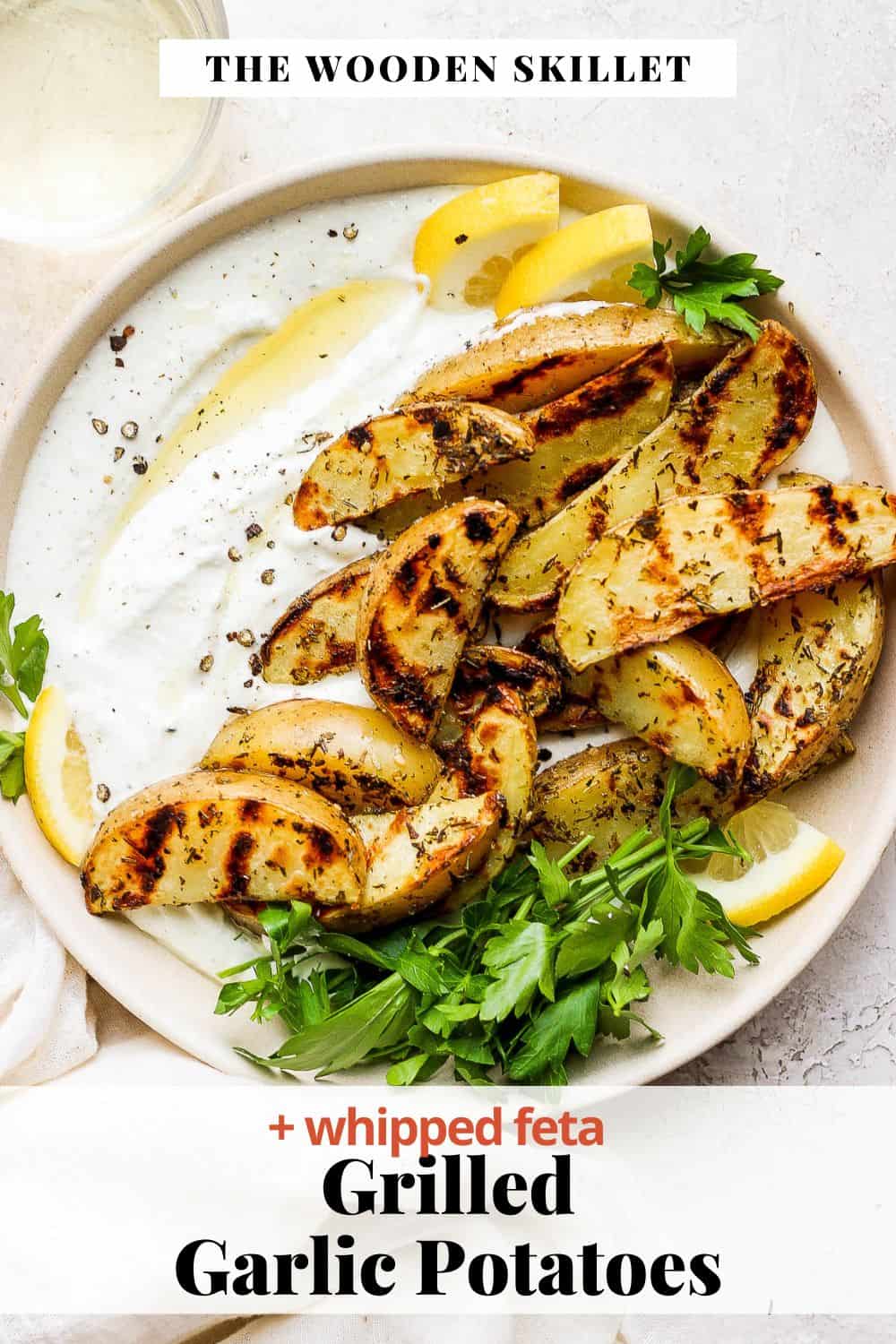 Pinterest image showing a bowl of whipped feta topped with garlic potatoes, lemon wedges, and fresh parsley.