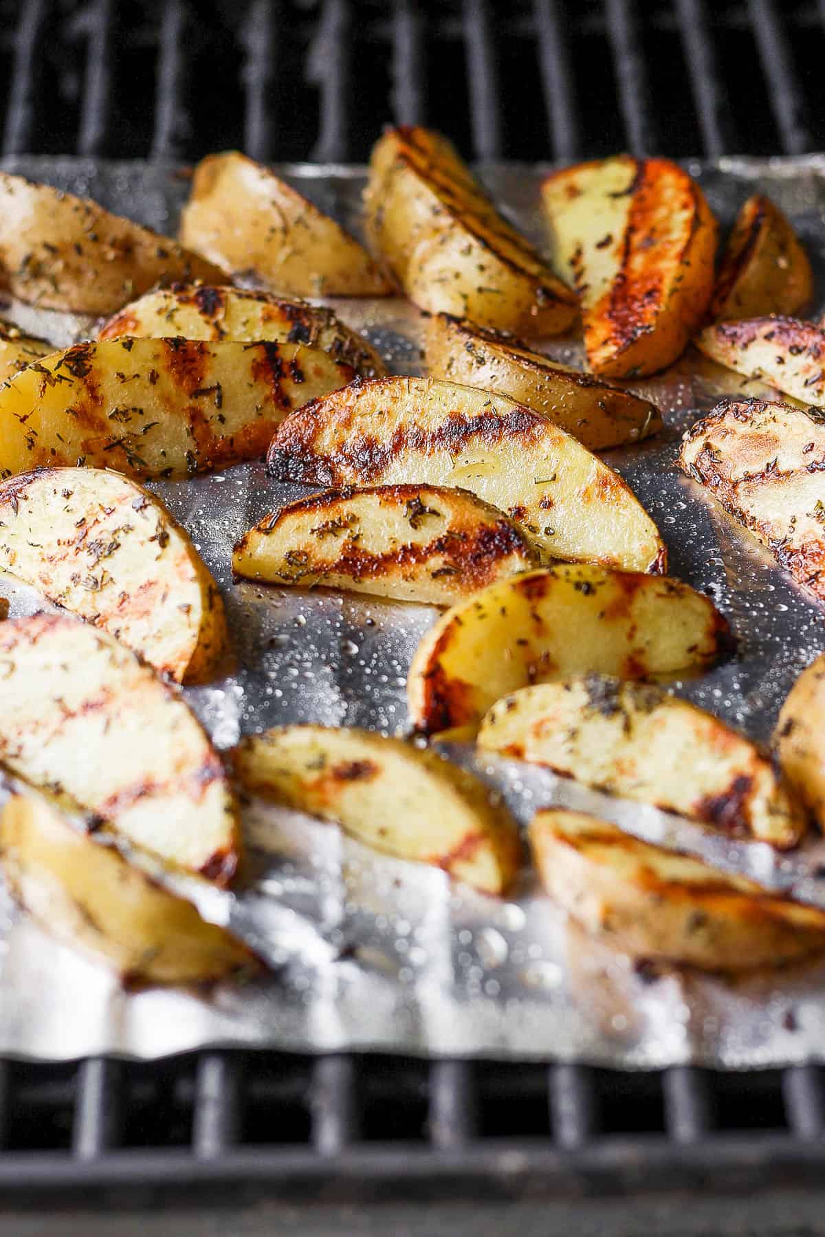 Roasted potato wedges on a tin foil sheet on the gril.