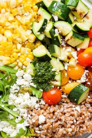 Top down shot of a grain salad with farro, grilled corn and zucchini, tomatoes, arugula and feta cheese.