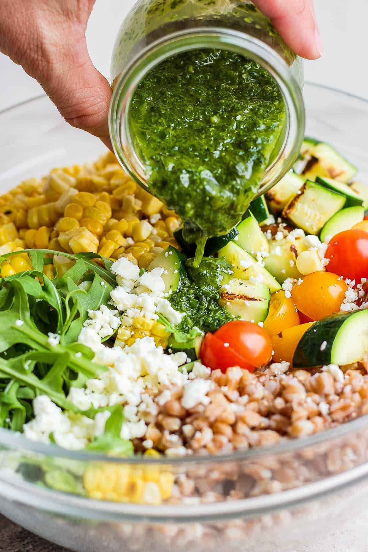 The basil vinaigrette being poured on the grain salad.