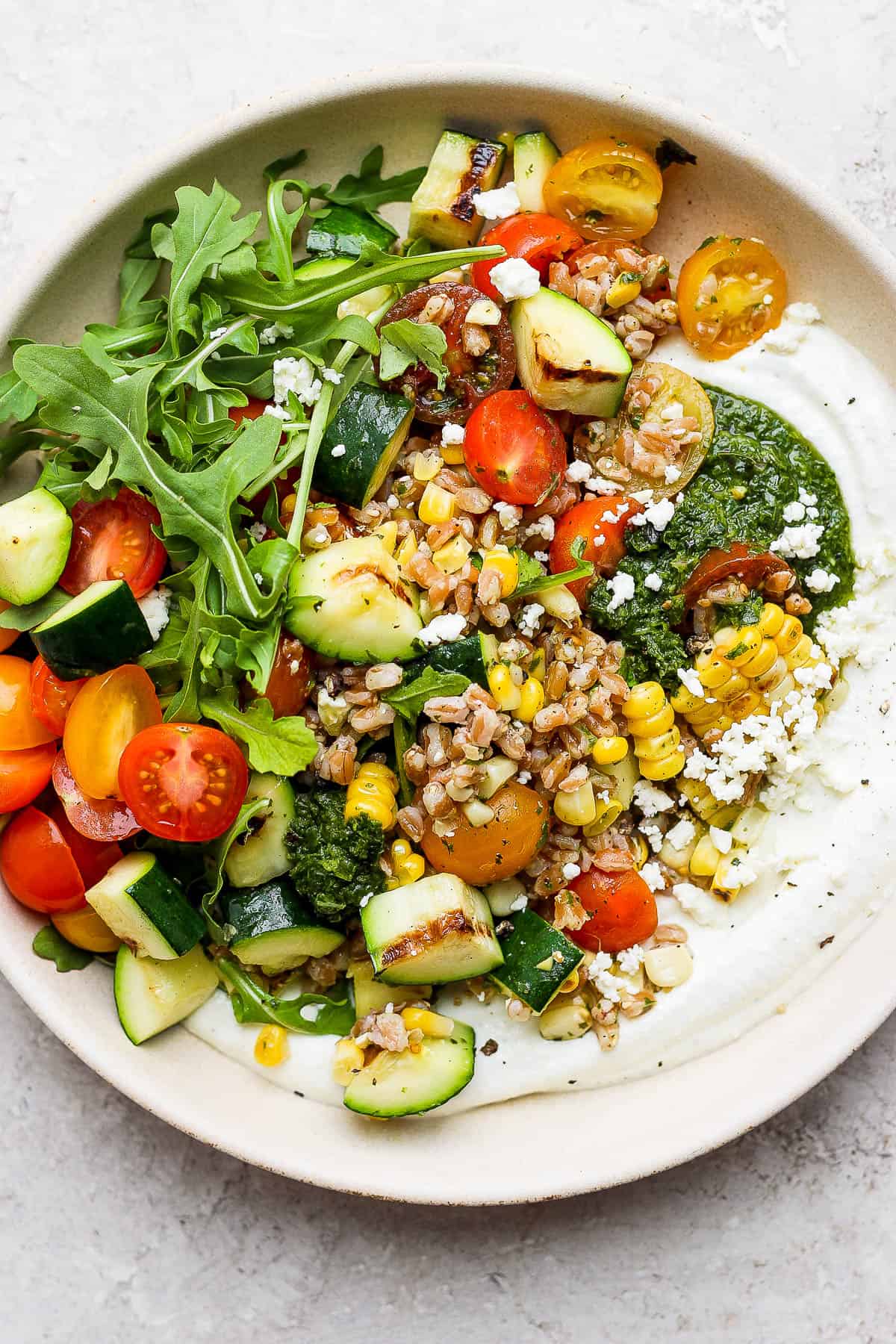 The summer grain salad served on top of some whipped feta in a shallow bowl.