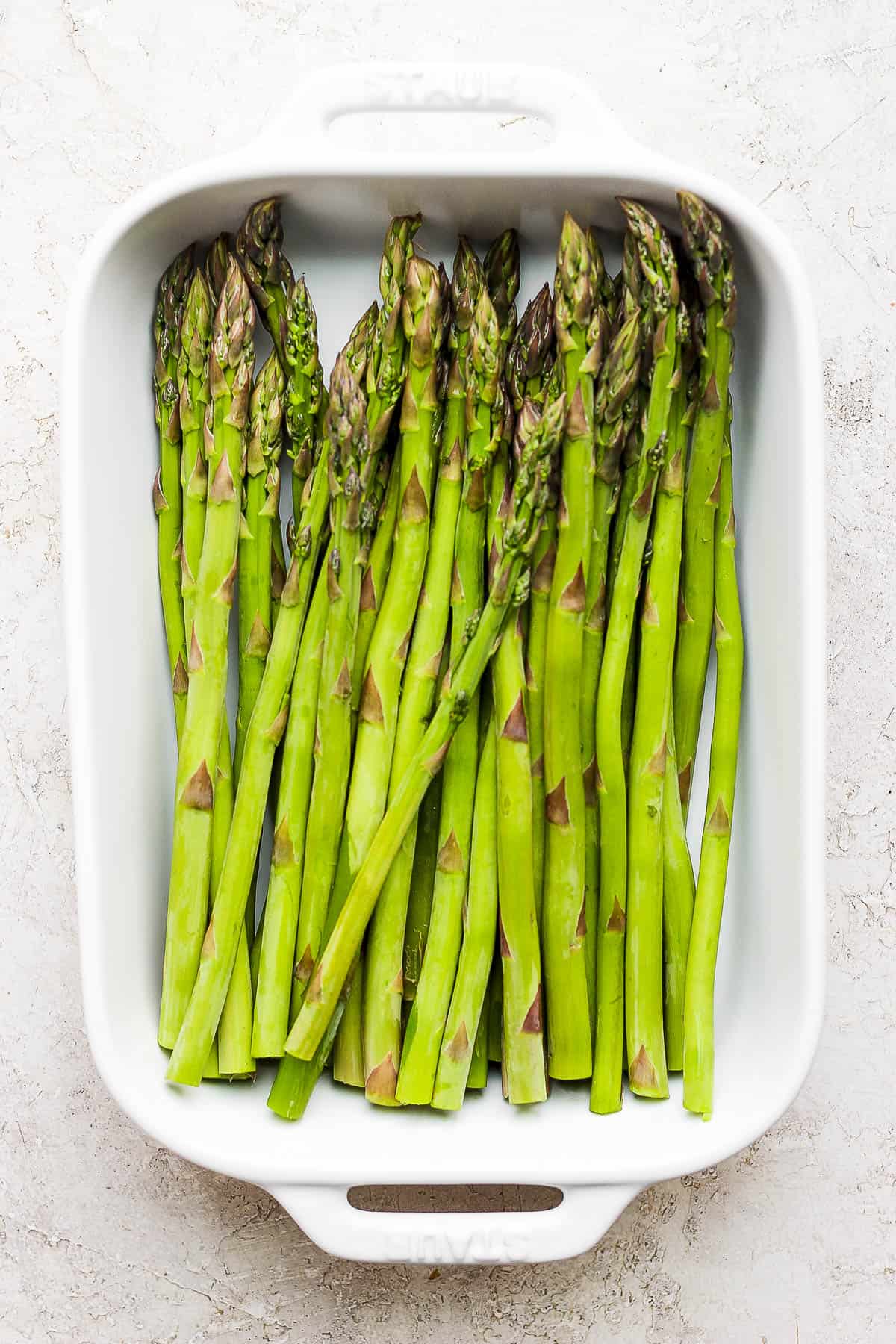 Trimmed asparagus stalks in a shallow, white baking dish.