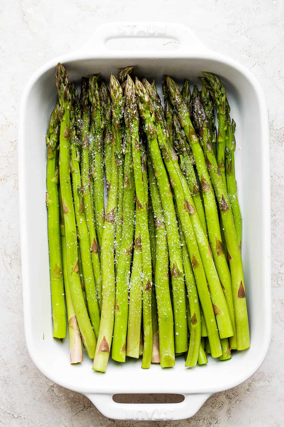 Oiled asparagus seasoned with salt and pepper in the baking dish.