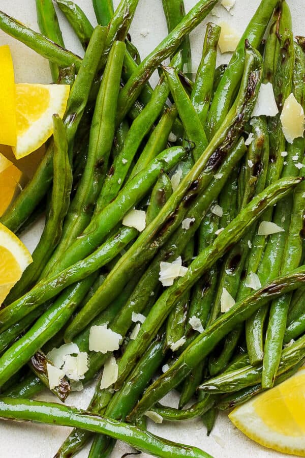 Plate of grilled green beans with lemon wedges and flakes parmesan cheese.