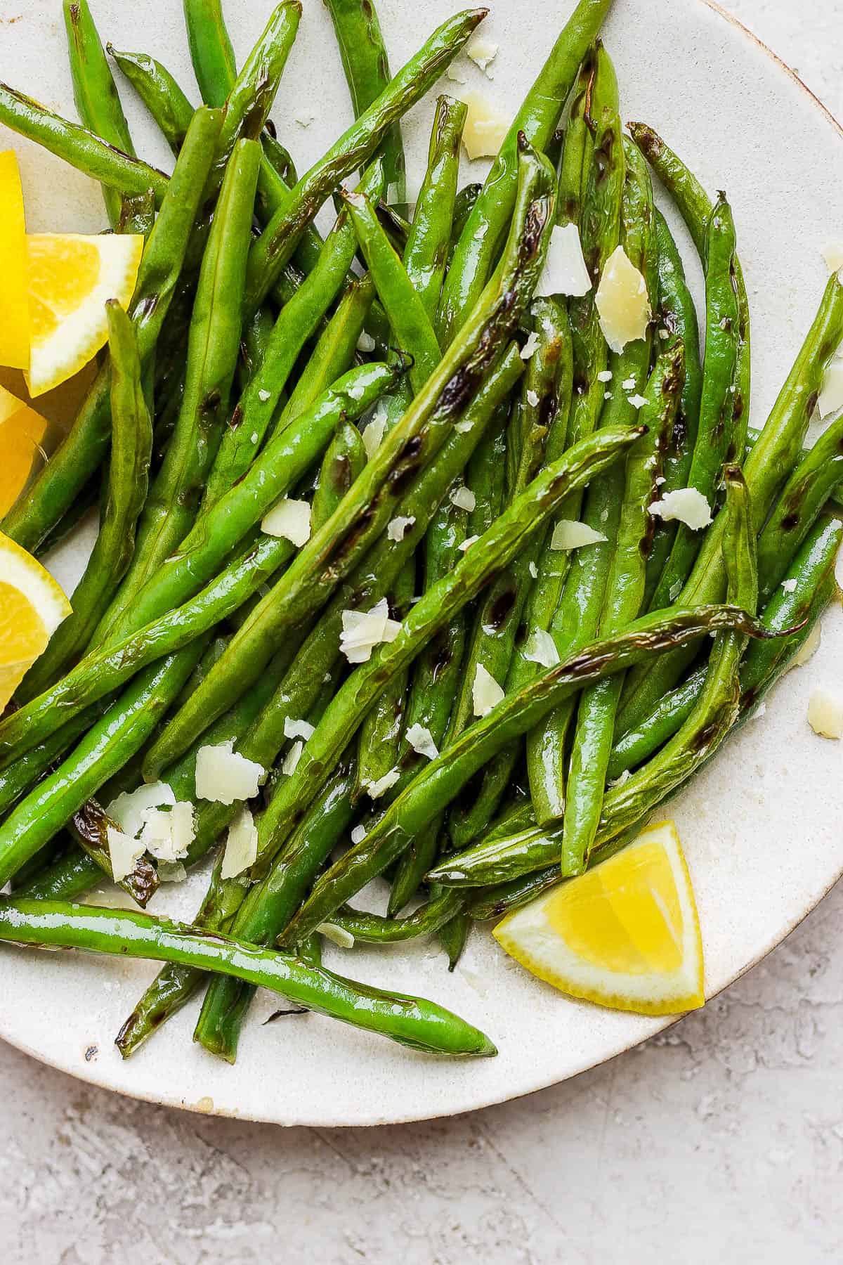 Grilled green beans topped with shaved parmesan and garnished with lemon wedges.