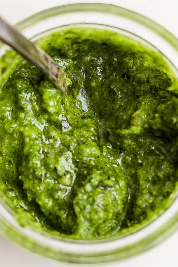 Top down shot of a jar of a homemade basil pesto recipe with a spoon sticking out.