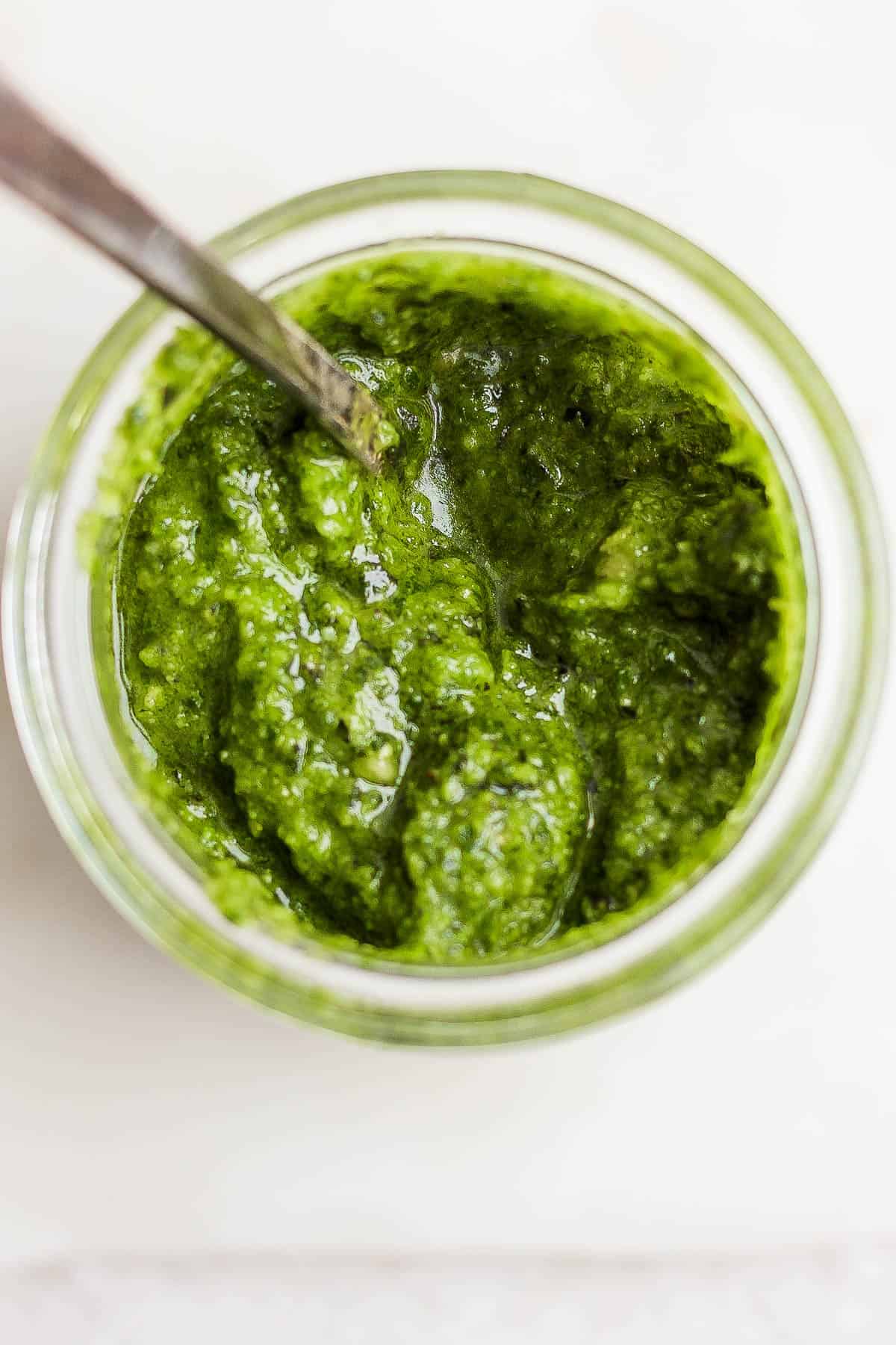 Basil pesto in a mason jar with a spoon.