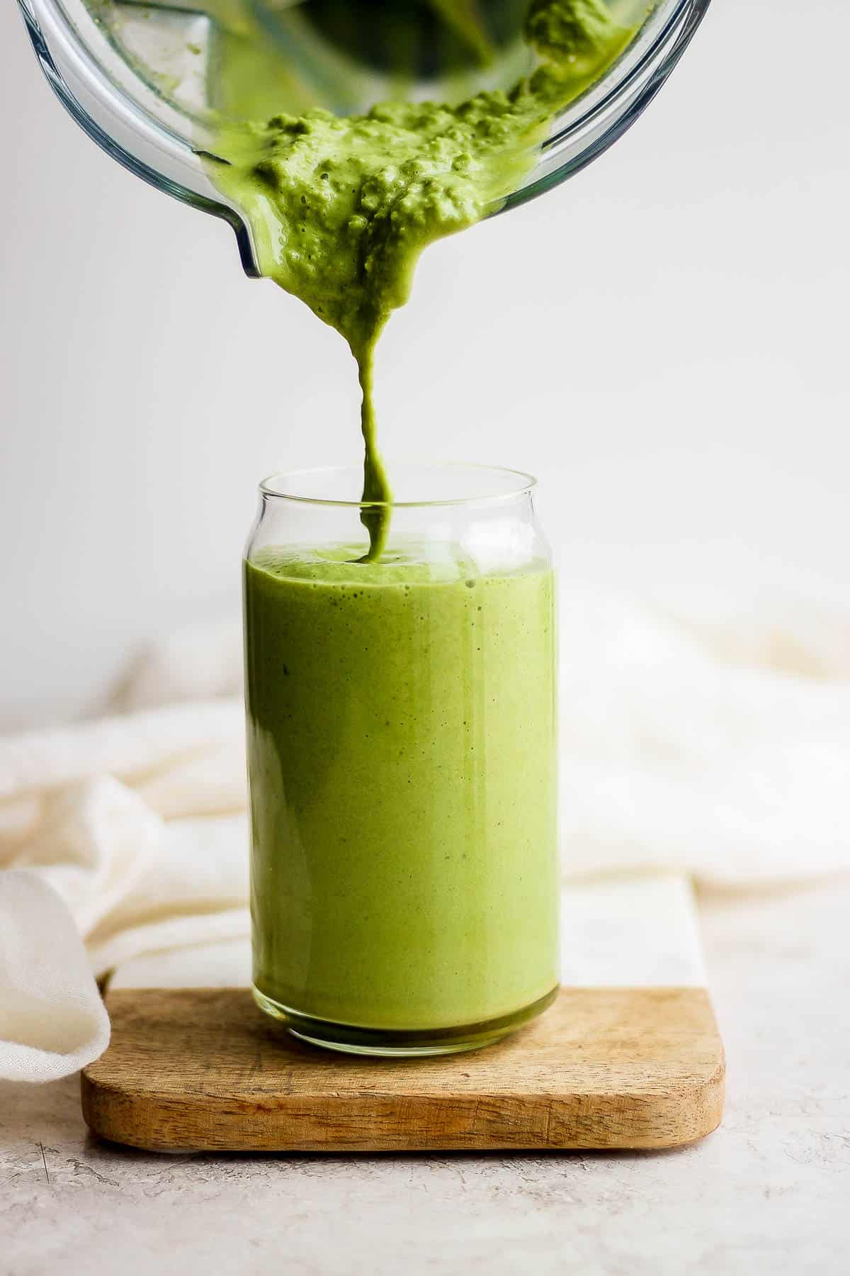 A matcha smoothie being poured into a tall glass.