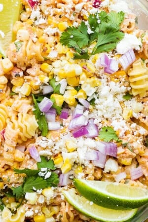 Top down shot of a glass bowl of mexican street corn pasta salad with lime wedges on top as well as chopped cilantro.