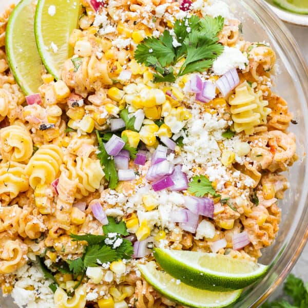 Top down shot of a glass bowl of mexican street corn pasta salad with lime wedges on top as well as chopped cilantro.