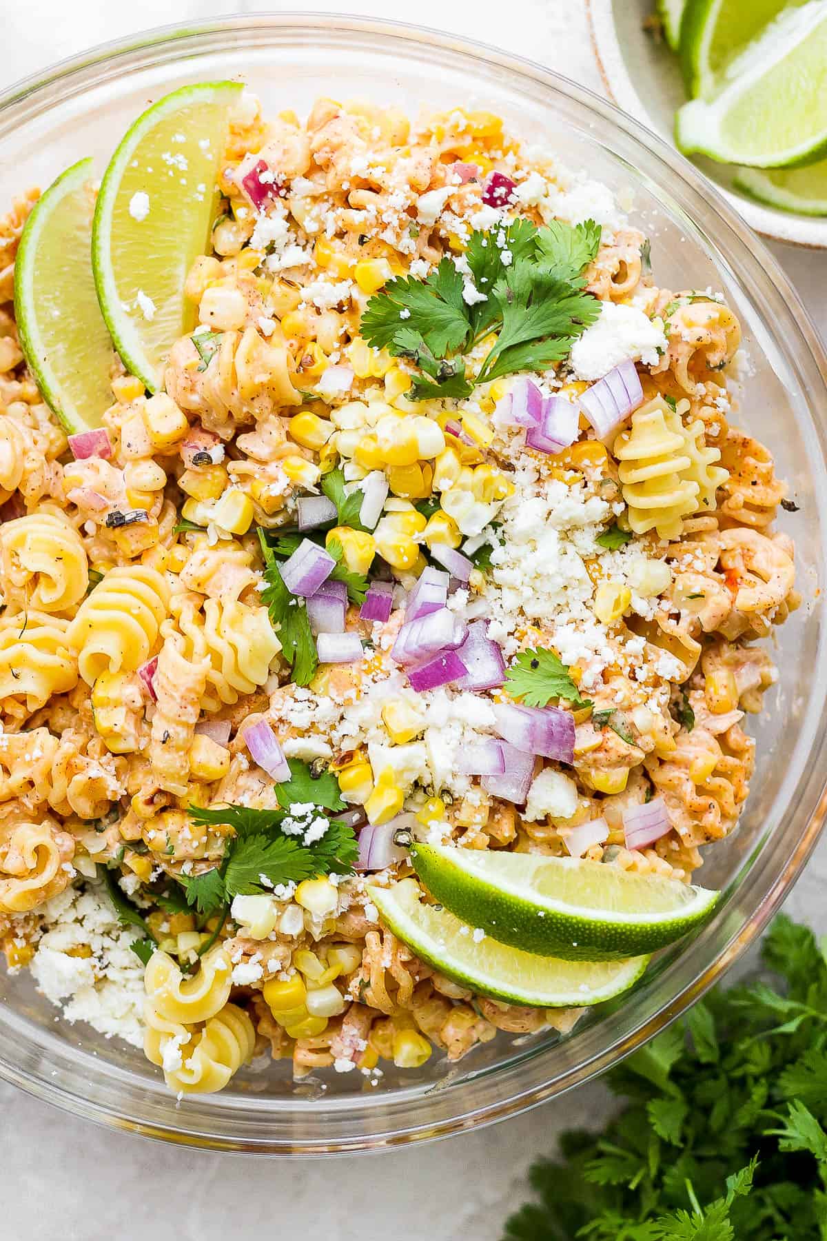 A bowl of mexican street corn pasta salad garnished with lime wedges and cilantro.