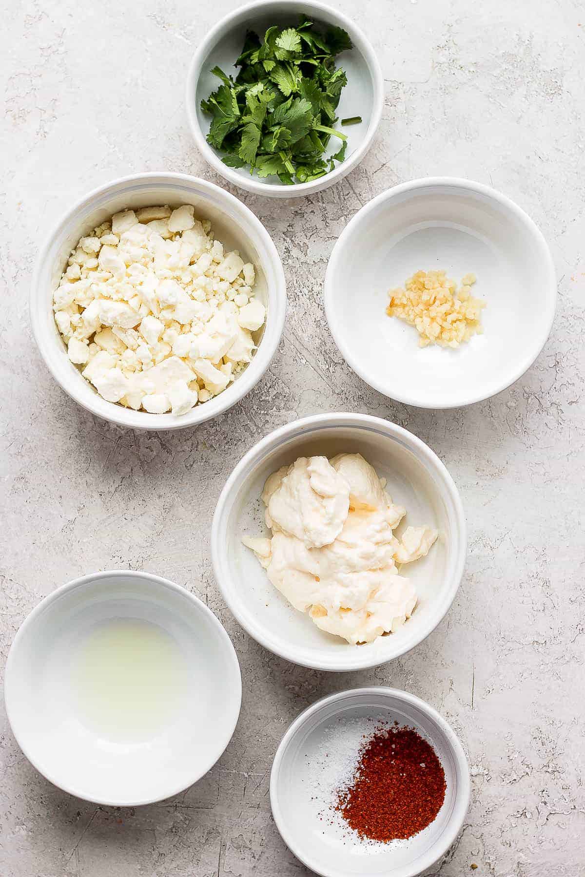 Individual bowls of cilantro, cojita cheese, minced garlic, mayo, lime juice, salt, and paprika.
