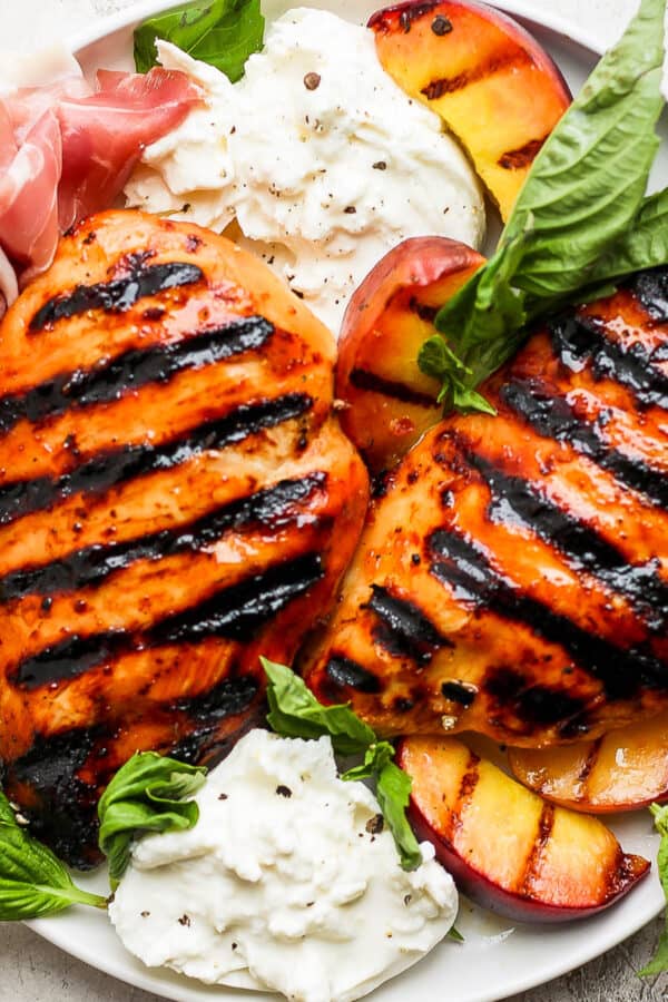 Grilled peach chicken on a plate with fresh basil, grilled peaches, fresh prosciutto and burrata cheese.