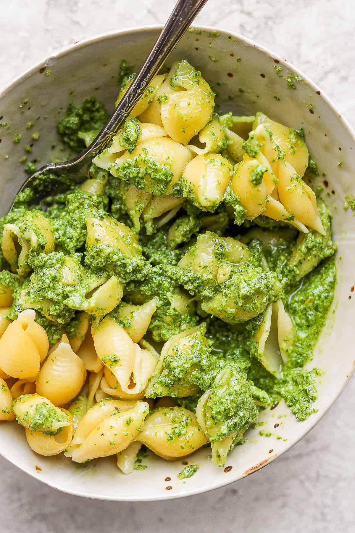 Basil pesto sauce covering all of the shells in the bowl.