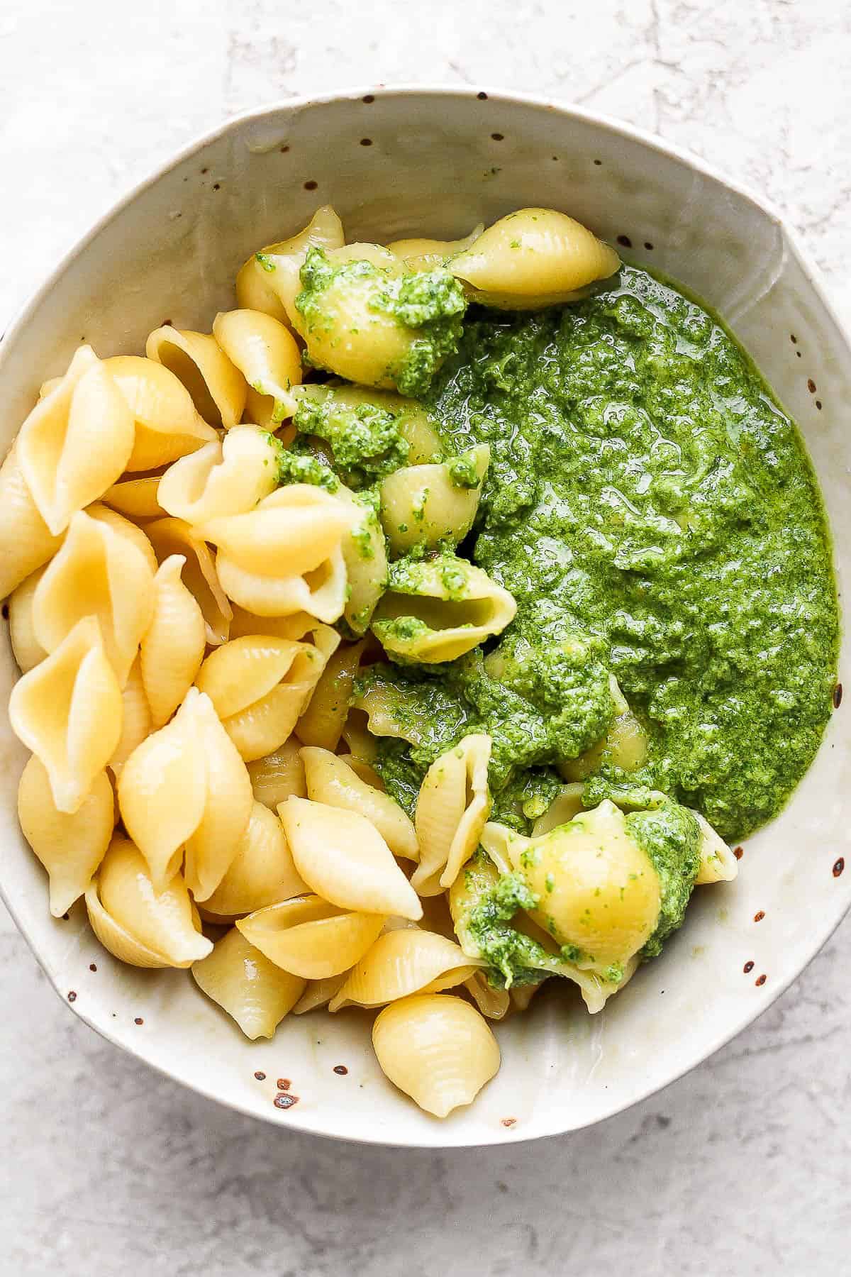 A bowl with cooked pasta shells and basil pesto sauce.