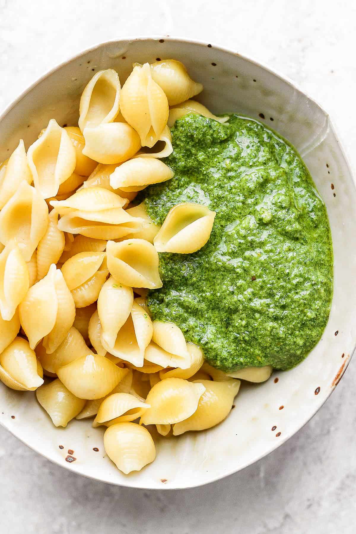 Cooked pasta shells and basil pesto in a bowl.