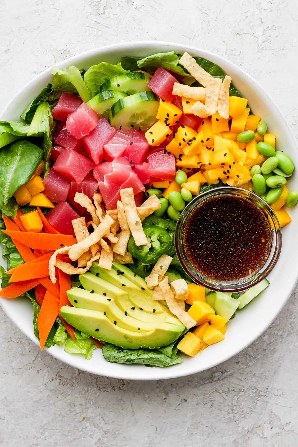 A tuna poke salad in a white bowl with a small bowl of dressing.