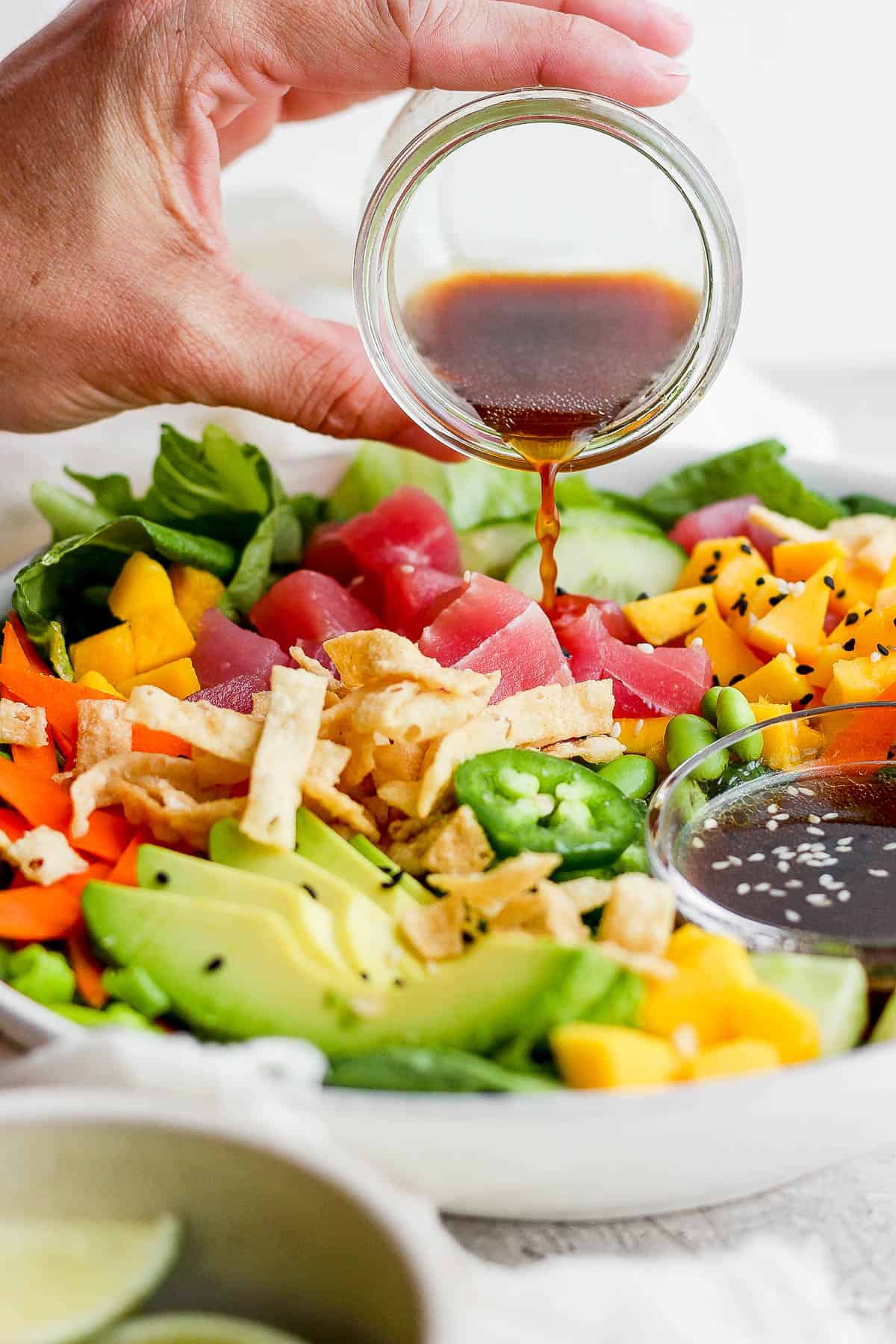 A hand pouring the sesame ginger dressing over the poke salad.