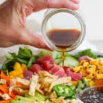 Someone pouring homemade sesame ginger dressing over a poke salad with tuna, mango and avocado.