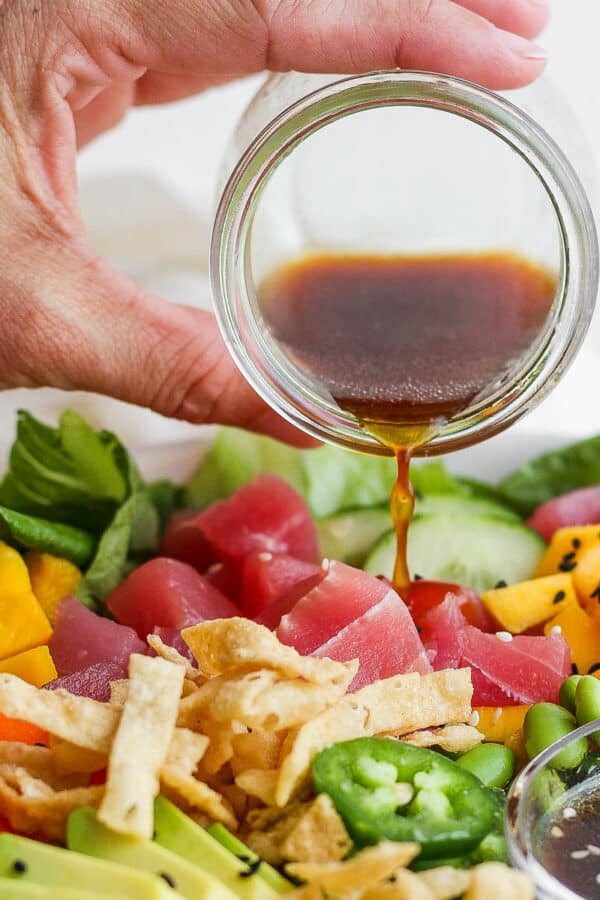 Someone pouring homemade sesame ginger dressing over a poke salad with tuna, mango and avocado.