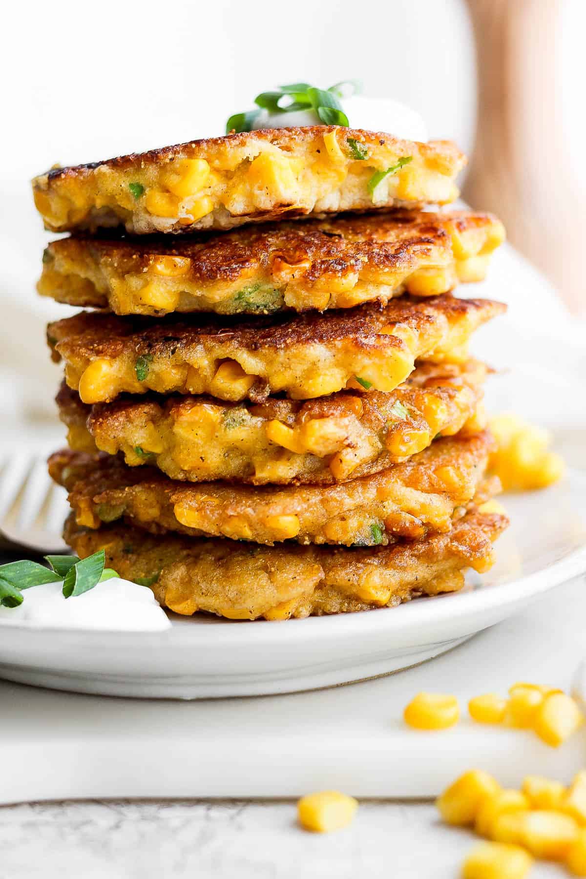 6 corn fritters stacked on a plate.