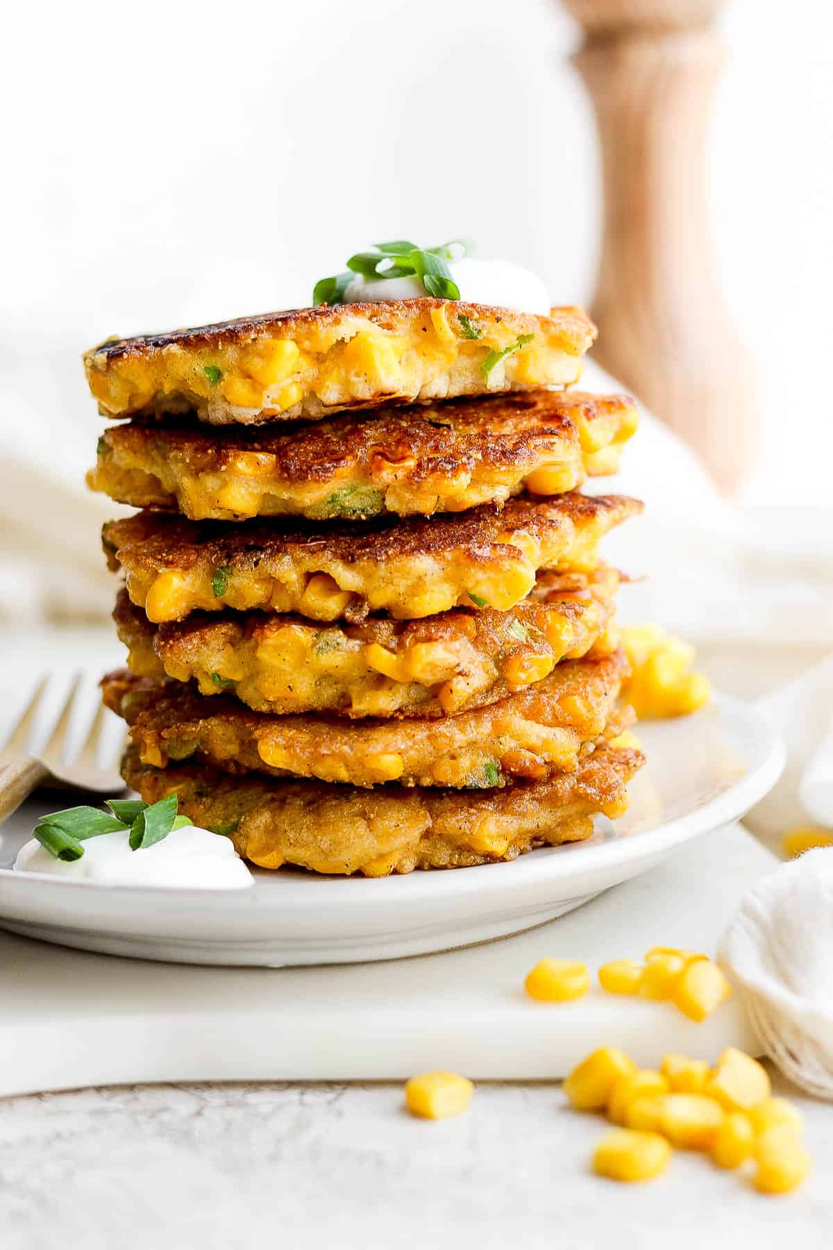 Six corn fritters stacked on top of each other on a plate.