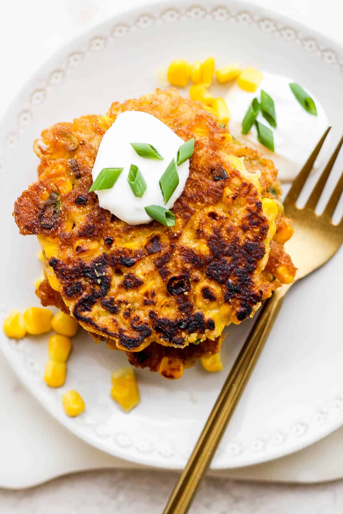 A dollop of sour cream mixture on a corn fritter on a plate with a fork next to it.