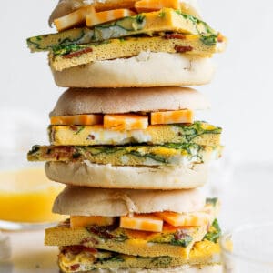 A stack of three freezer breakfast sandwiches with cheese in english muffins.