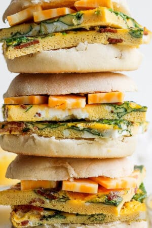 A stack of three freezer breakfast sandwiches with cheese in english muffins.