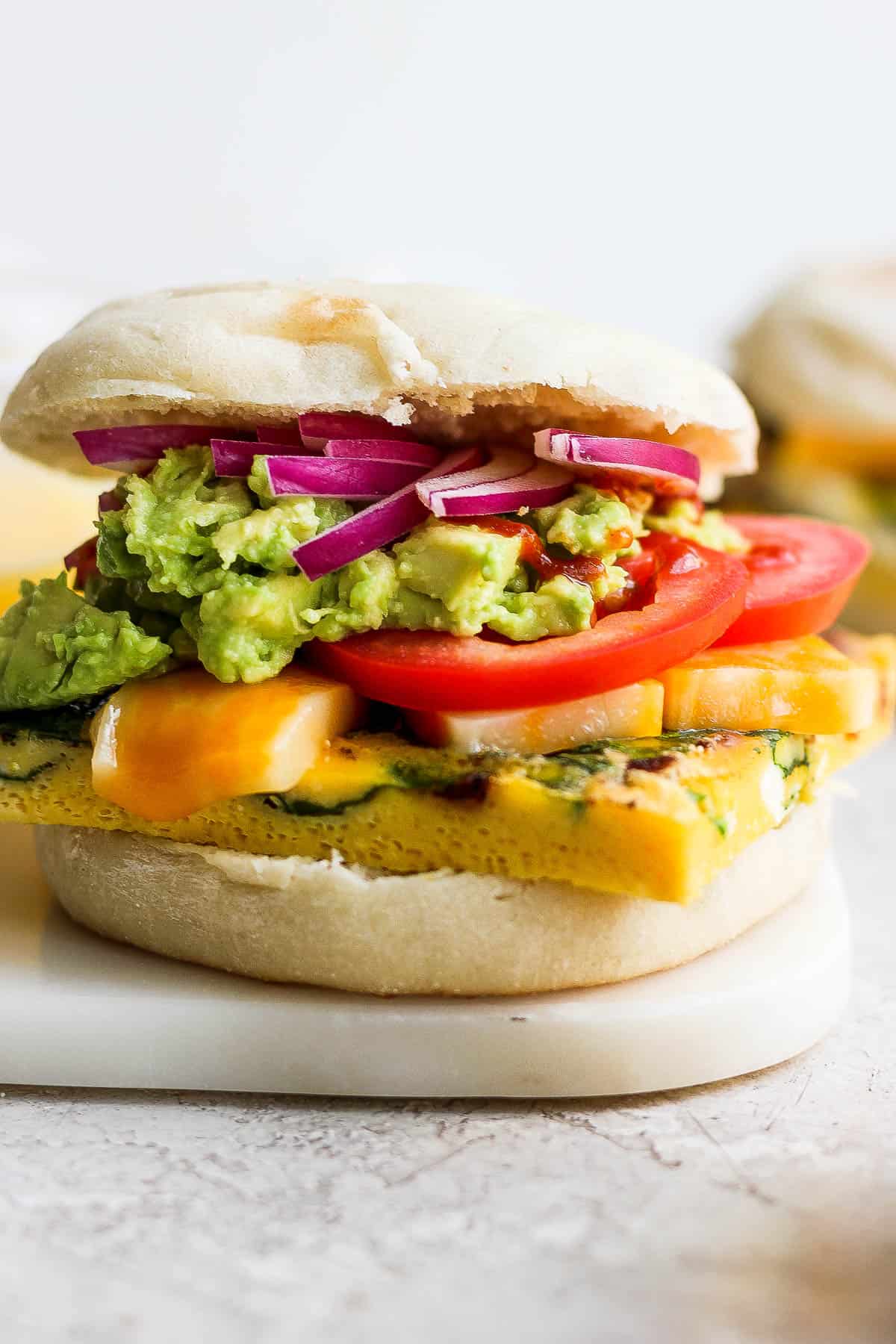 A reheated breakfast sandwich with tomato, avocado, and red onion on top.