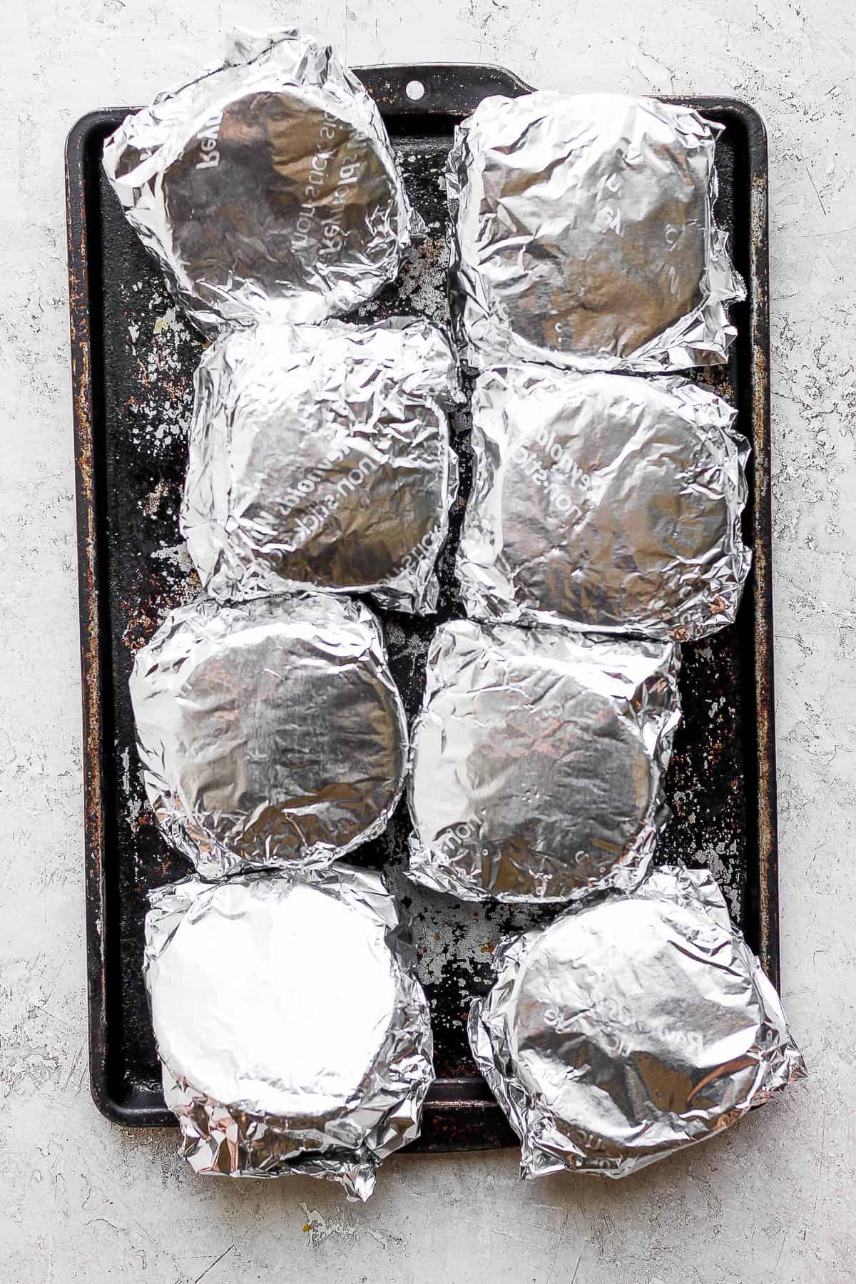 Fully foil-wrapped breakfast sandwiches on a baking sheet.