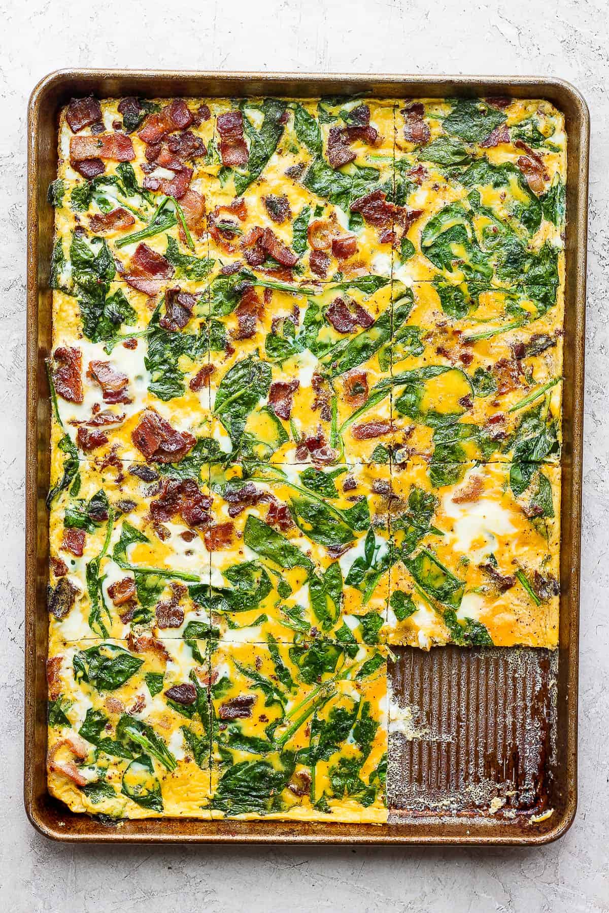 The egg mixture in the pan after baking and being cut into squares with one of them removed.