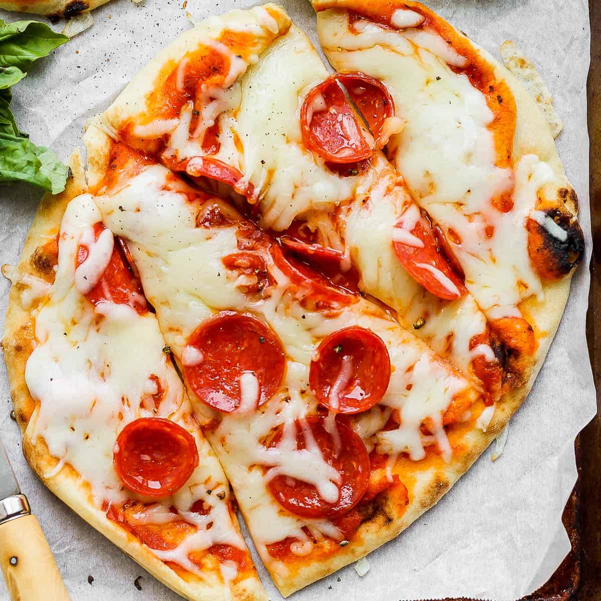 A sliced naan pizza on piece of parchment paper.