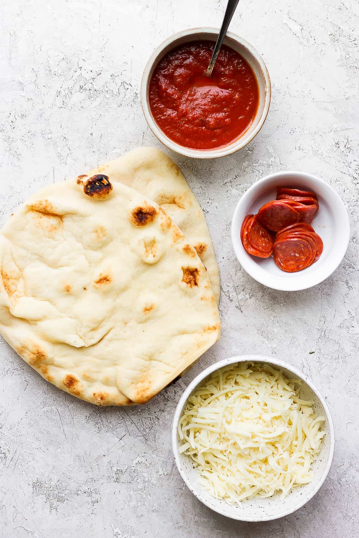 Ingredients on the counter for a pepperoni naan pizza.