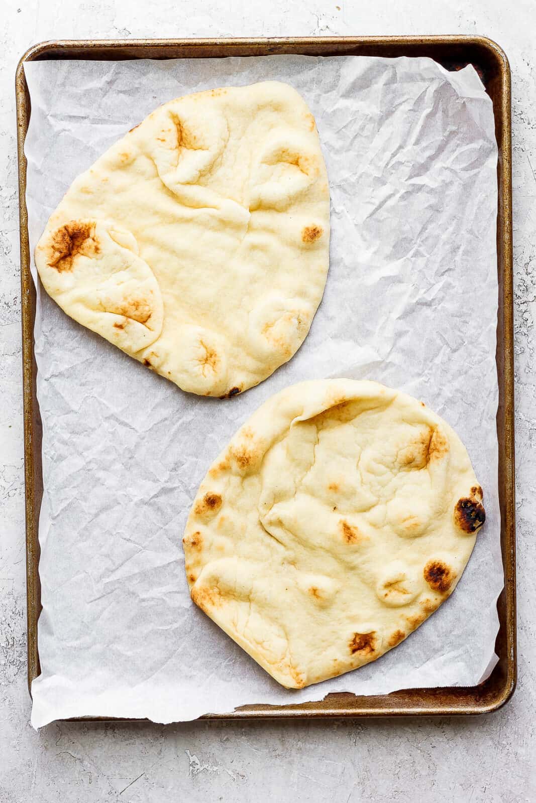 Two pieces of naan flatbread on a baking sheet lined with parchment paper to make naan flatbread pizza.