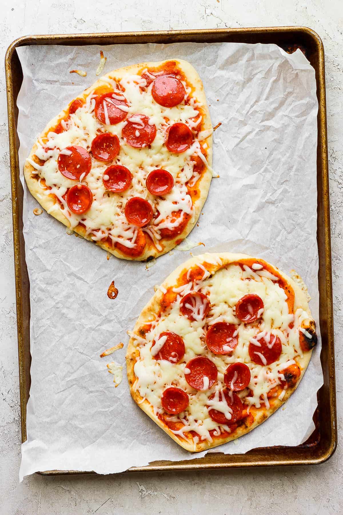 A baking sheet with two naan pizzas after baking.