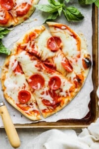 Naan flatbread pizza cut into triangles on a plate.
