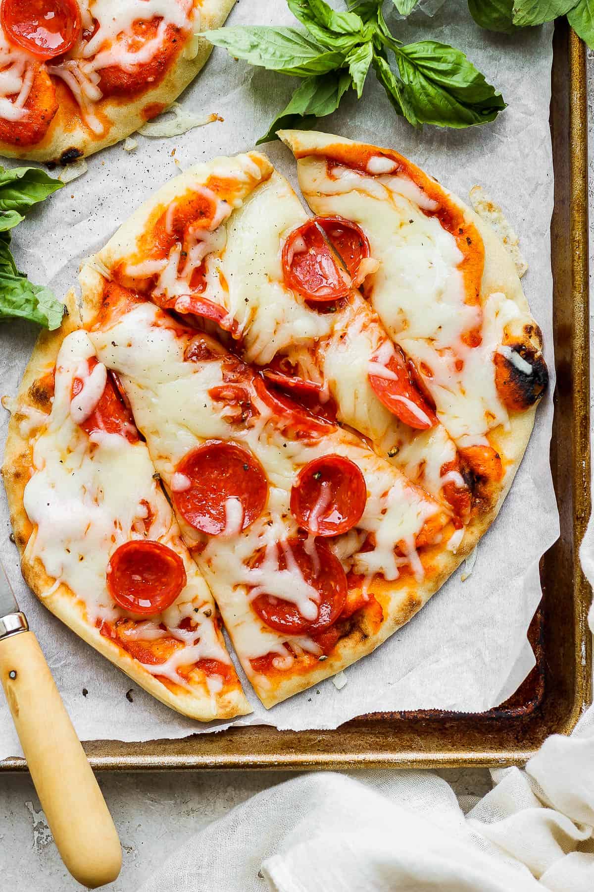 A close-up shot of a naan pizza cut into slices on the baking sheet.