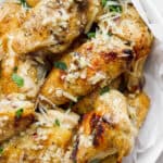 A bowl lined with parchment filled with garlic parmesan wings topped with extra shredded parmesan and fresh parsley.